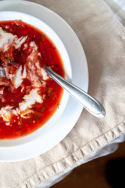 Traditional Ukrainian-Russian tomato borscht soup with sour cream in a white plate on the table. View from above. — Stock Photo, Image