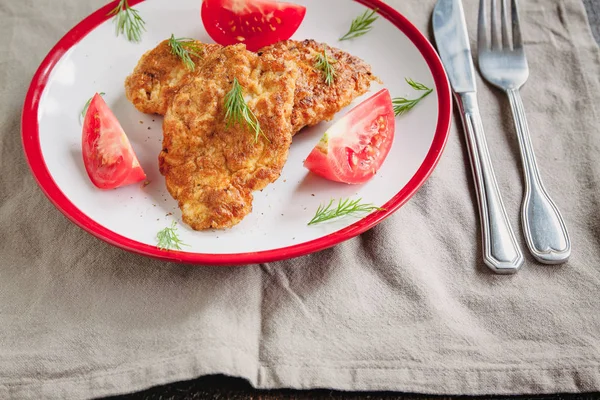 juicy meat-chicken chops and tomatoes on a white plate on a simple light linen background served with a fork and knife