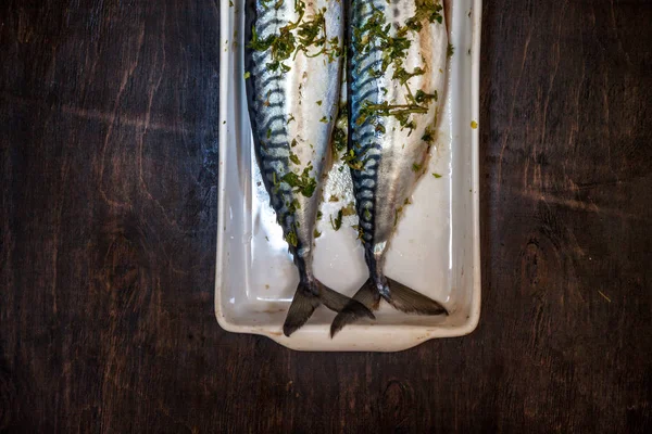 Deux poissons crus maquereau dans les verts et les herbes seront cuits sur un fond sombre. Vue d'en haut. Effet rétroactif — Photo