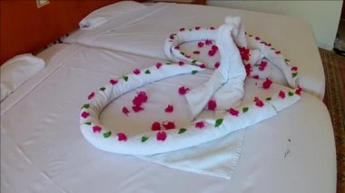 kalp ve otelde yatakta pembe çiçeklerile havlu yapılmış kuğu.