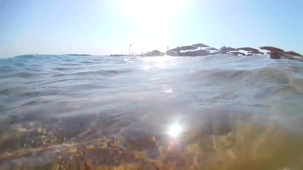 かさぶたの傘とデッキチェア 超広い丸いコーナーで海岸近くのサーフの波に揺れるカメラからのビデオ スローモーション標準移動 — ストック動画
