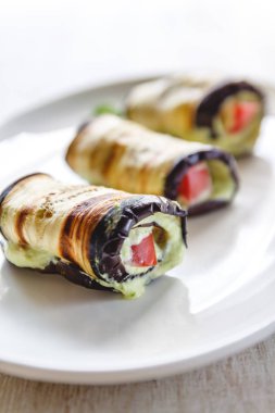 hafif bir arka plan üzerinde beyaz bir tabak üzerinde kızarmış patlıcan, süzme peynir ve domates geleneksel çanak üç rulo. Minimalizm. Yukarıdan görüntüle