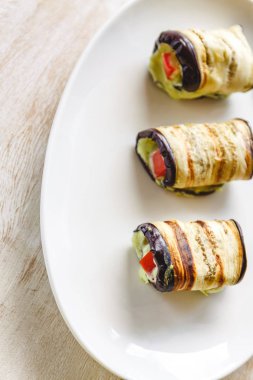 hafif bir arka plan üzerinde beyaz bir tabak üzerinde kızarmış patlıcan, süzme peynir ve domates geleneksel çanak üç rulo. Minimalizm. Yukarıdan görüntüle