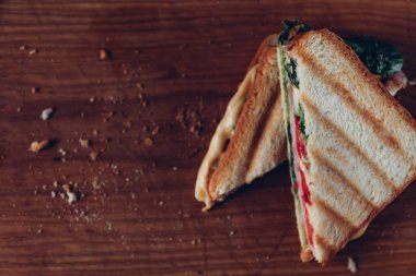 Ahşap arka planda iki sandviç, üst görünüm. Bir kesme tahtasında jambon, peynir ve marul sandviç ile Panini yığını