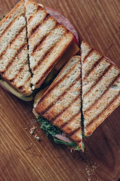 Twee broodjes op een houten achtergrond, Top uitzicht. Een stapel Panini met ham, kaas en sla sandwich op een snijplank — Stockfoto