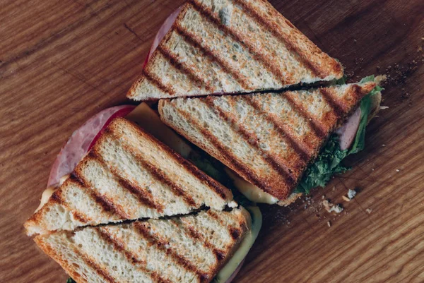 Ahşap arka planda iki sandviç, üst görünüm. Bir kesme tahtasında jambon, peynir ve marul sandviç ile Panini yığını — Stok fotoğraf