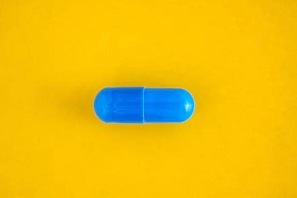 Uma cápsula pílula azul isolada no fundo amarelo, close-up, vista superior, espaço de cópia — Fotografia de Stock