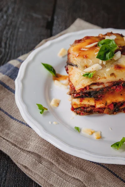 Tradicional Parmigiana di melanzane: berinjela assada - itália, cousina da Sicília. Berinjela assada com queijo, tomates e especiarias em um prato branco. Um prato de berinjela está em uma mesa de madeira — Fotografia de Stock