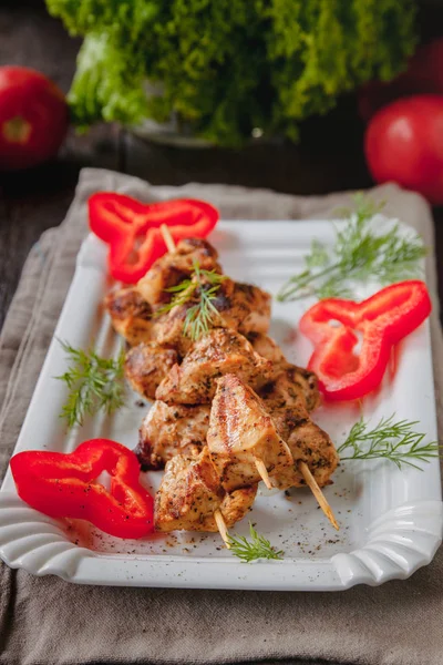 Juicy meat-chicken skewers on wooden skewers on a white plate on a dark wooden background — Stock Photo, Image