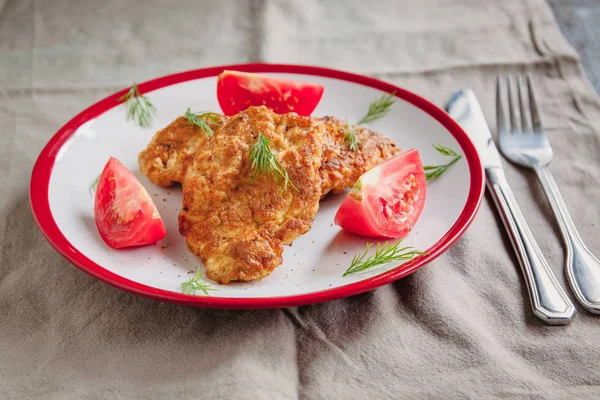 juicy meat-chicken chops and tomatoes on a white plate on a simple light linen background served with a fork and knife