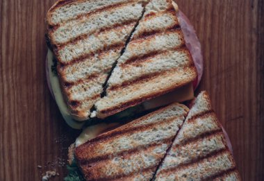 Ahşap arka planda iki sandviç, üst görünüm. Bir kesme tahtasında jambon, peynir ve marul sandviç ile Panini yığını
