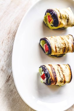 hafif bir arka plan üzerinde beyaz bir tabak üzerinde kızarmış patlıcan, süzme peynir ve domates geleneksel çanak üç rulo. Minimalizm. Yukarıdan görüntüle