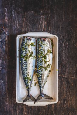 Yeşiller ve otlar iki çiğ balık uskumru karanlık bir arka planda pişmiş olacak. Yukarıdan görüntüle. Retro etkisi