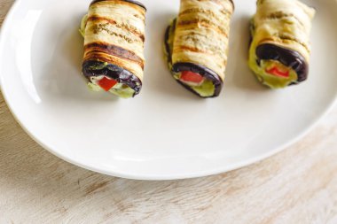 hafif bir arka plan üzerinde beyaz bir tabak üzerinde kızarmış patlıcan, süzme peynir ve domates geleneksel çanak üç rulo. Minimalizm. Yukarıdan görüntüle