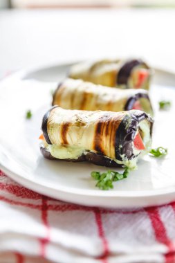 hafif bir arka plan üzerinde beyaz bir tabak üzerinde kızarmış patlıcan, süzme peynir ve domates geleneksel çanak üç rulo. Minimalizm. Yukarıdan görüntüle