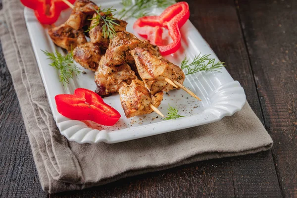 juicy meat-chicken skewers on wooden skewers on a white plate on a dark wooden background
