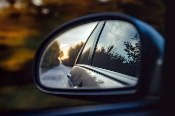 Reflektion av vägen i solnedgången solljus suddiga i sido spegeln av bilen. Närbild — Stockfoto