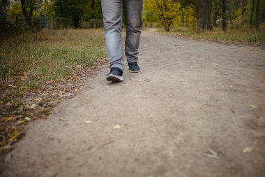 Kot pantolonlu ve spor ayakkabılı erkek bacakları yere doğru yürüyordu. Her tarafı sarı yapraklarla kaplıydı. Sonbahar varış konsepti, yakın plan, kopyalama alanı.