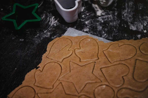 cut out gingerbread cookie in the form of a Christmas tree, star, little man, hearts from raw dough on parchment baking paper on a dark background. Top view. save space