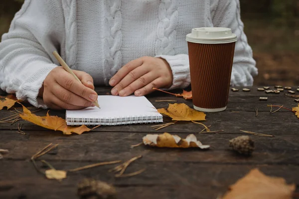 人的手与一杯咖啡和围巾在木制桌子与笔记本电脑，钢笔和秋天的叶子。 人的手，与一杯咖啡和围巾在木制桌子旁 — 图库照片