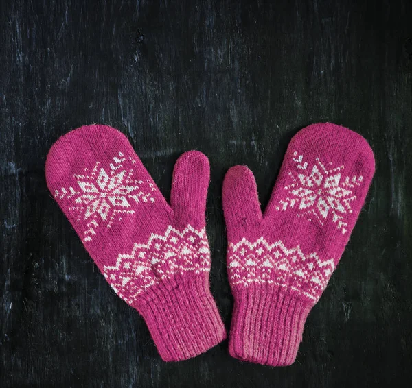 Ein Paar rot-rosa-lila-magenta lila Strickhandschuhe auf einem dunkelblau-grün-braunen Holz — Stockfoto