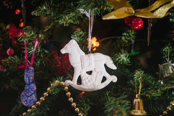 Brinquedos de Natal na forma de um cavalo de balanço antigo de cerâmica branca com presentes em uma árvore de Natal decorada. Close-up . — Fotografia de Stock