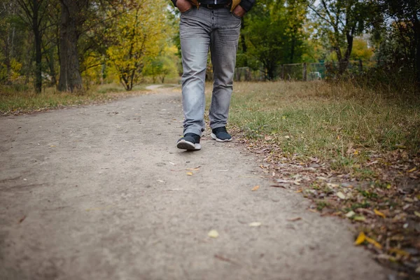 Jambes masculines en jean et baskets marchant au loin sur le sol recouvert de feuilles jaunes tombées. Concept d'arrivée d'automne, gros plan, espace de copie . — Photo