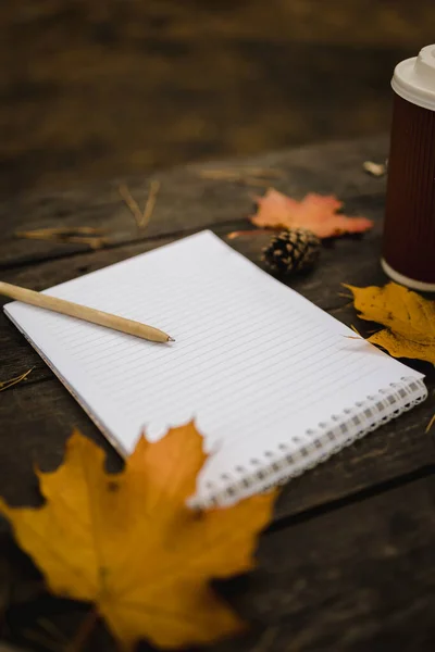 白い空白のノートとスカーフ、演奏とカップ、秋の黄色の葉と周りの松のコーンと暗い背景にペン。上からの眺め。フラットレイ、ぼやけてスペースのコピー ロイヤリティフリーのストック画像
