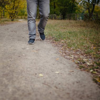 Kot pantolonlu ve spor ayakkabılı erkek bacakları yere doğru yürüyordu. Her tarafı sarı yapraklarla kaplıydı. Sonbahar varış konsepti, yakın plan, kopyalama alanı.