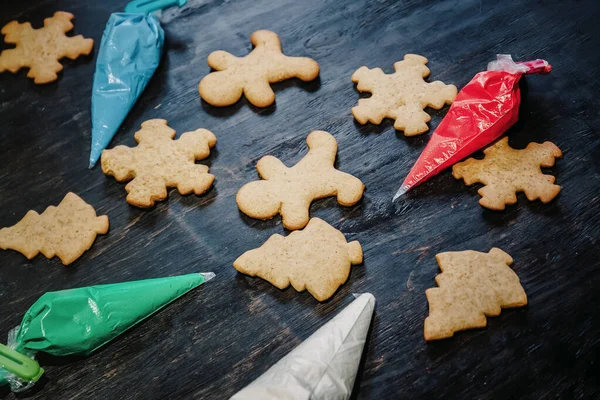 Zdobit vánoční perník cookies pomocí barevné glazury na tmavém dřevěném stole, horní pohled — Stock fotografie