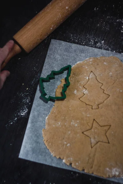 Corten la forma de la galleta de jengibre en forma del árbol de Navidad de la masa cruda sobre el papel de hornear pergamino sobre el fondo oscuro. Vista desde arriba. ahorrar espacio — Foto de Stock