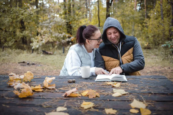 Beau couple amoureux assis sur le banc dans le parc d'automne à lire un livre, s'amuser ensemble. Amour et tendresse. Relations, amitiés, éducation, mode de vie concept — Photo