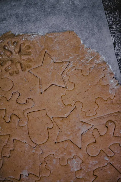Вирізане імбирне печиво у вигляді ялинки, зірки, маленького чоловічка, серця з сирого тіста на пергаменті на темному фоні. Вид зверху. зберегти простір — стокове фото