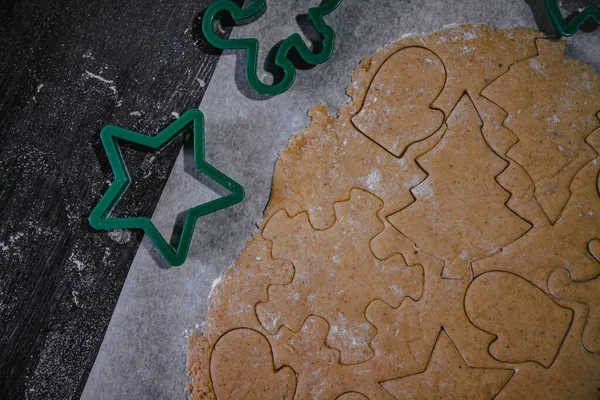 Cut out gingerbread cookie in the form of a Christmas tree, star, little man, hearts from raw dough on parchment baking paper on a dark background. Top view. save space — Stock Photo, Image
