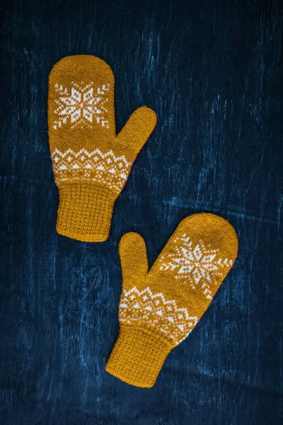 A pair of yellow orange knitted mittens on a dark blue-green-brown wooden — Stock Photo, Image