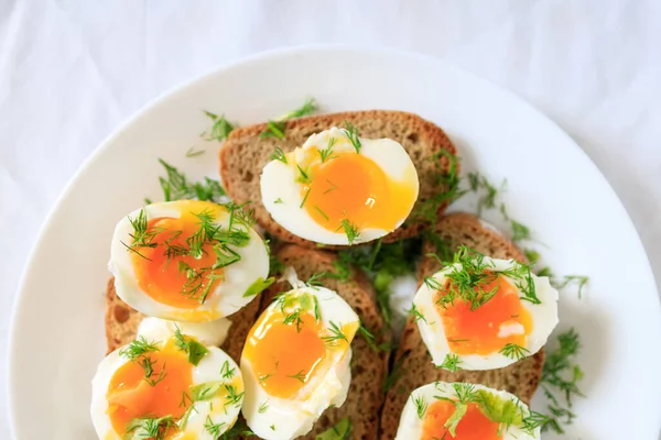 Metades de ovo macio-fervidas com endro em pão de grão inteiro torrado em uma chapa branca. Close-up, vista superior. Conceito de pequeno-almoço saudável, saudável e saudável . — Fotografia de Stock