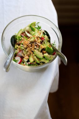 Şeffaf bir kâse avokadoda salata, ceviz, yeşil salata, masasında beyaz bir masa örtüsü olan turplu Fransız hardalı. Yukarıdan görüntüle