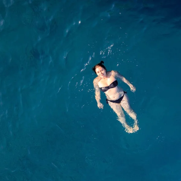 Воздушный вид сверху счастливая молодая женщина в черном купальнике плавает в Красном море, Египет, Шарм-эль-Шейх. Отдых и приключения. Голубая вода. Вид сверху на ленивую девушку, отдыхающую в море-океане. Копирование пространства — стоковое фото