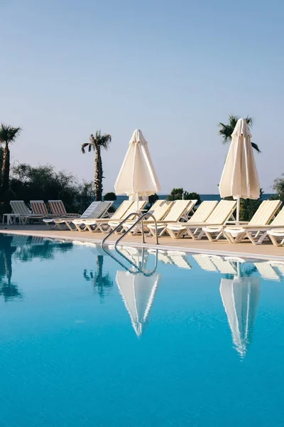 Vista de la piscina, tumbonas y sombrillas entre exuberantes palmeras verdes y arbustos en la suave luz de la mañana en un hotel resort en Alanya, Turquía — Foto de Stock