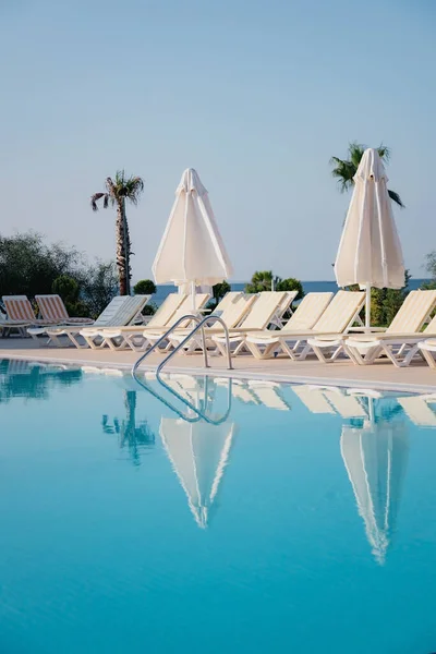 Vista de la piscina, tumbonas y sombrillas entre exuberantes palmeras verdes y arbustos en la suave luz de la mañana en un hotel resort en Alanya, Turquía — Foto de Stock