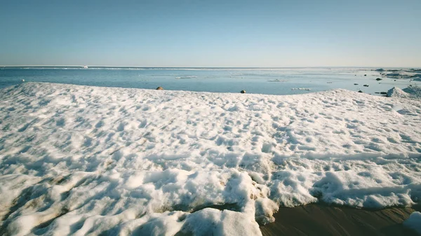 Snow pile, hill. Large snow drift isolated on a blue sky background, outdoor view of ice blocks at frozen finland lake in winter