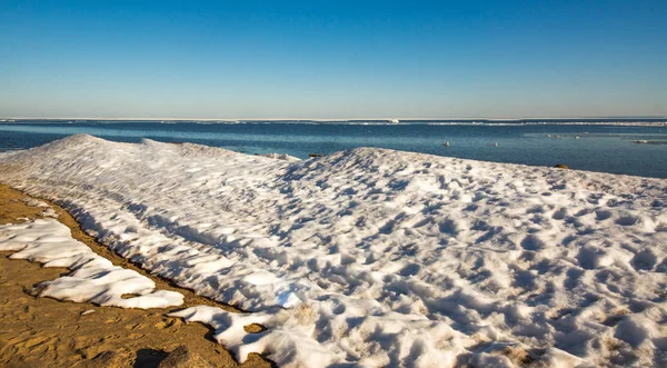 Snow pile on the beach, hill. Large snow drift isolated on a blue sky background, outdoor view of ice blocks at frozen finland lake in winter