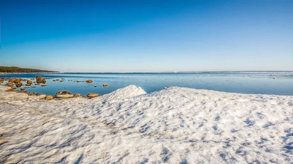 Snow pile, hill. Large snow drift isolated on a blue sky background, outdoor view of ice blocks at frozen finland lake in winter