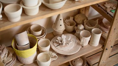Kil kaplar için raflar ile Raf. Çizim ve çömlek boyama için fırçalar. Bir çömlekçinin elinde çiğ kil bir tencere. Çömlek atölyesinde atölye