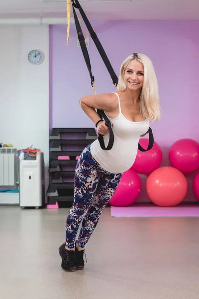 Joven embarazada atractiva mujer de entrenamiento con correas de fitness trx en el estudio de gimnasios — Foto de Stock