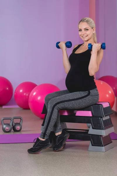 Deportiva mujer rubia embarazada haciendo ejercicio con pesas en 9 meses de embarazo con placer — Foto de Stock