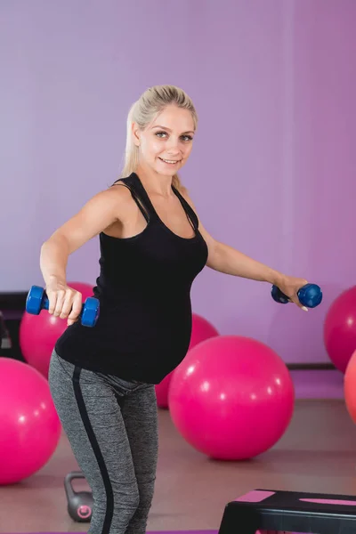 Mujer embarazada de pie en el gimnasio, sosteniendo sus pesas en 9 meses con hermosa vista y haciendo ejercicio sobre hombros y brazos — Foto de Stock