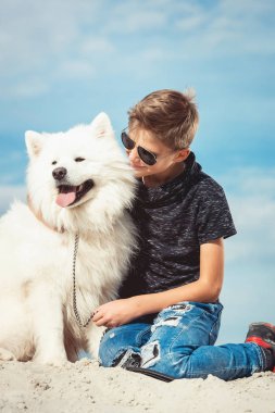 Mutlu 11 yaşında bir çocuk ile oynarken onun köpek doğurmak Samoyed, deniz kıyısı mavi gökyüzü karşı kapatın. Arkadaşlar diğer en iyi ve eğlenceli tatile, kuma oyun