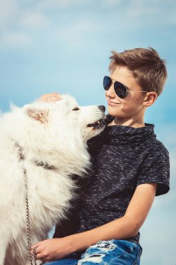 Mutlu 11 yaşında bir çocuk ile oynarken onun köpek doğurmak Samoyed, deniz kıyısı mavi gökyüzü karşı kapatın. Arkadaşlar diğer en iyi ve eğlenceli tatile, kuma oyun