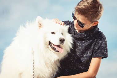 Mutlu 11 yaşında bir çocuk ile oynarken onun köpek doğurmak Samoyed, deniz kıyısı mavi gökyüzü karşı kapatın. Arkadaşlar diğer en iyi ve eğlenceli tatile, kuma oyun